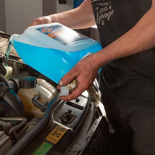 Manos de hombre sujetando una bombona de líquido refrigerante sobre un motor